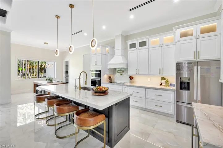 Kitchen featuring stainless steel fridge, white cabinetry, light stone counters, glass insert cabinets, and a breakfast bar area