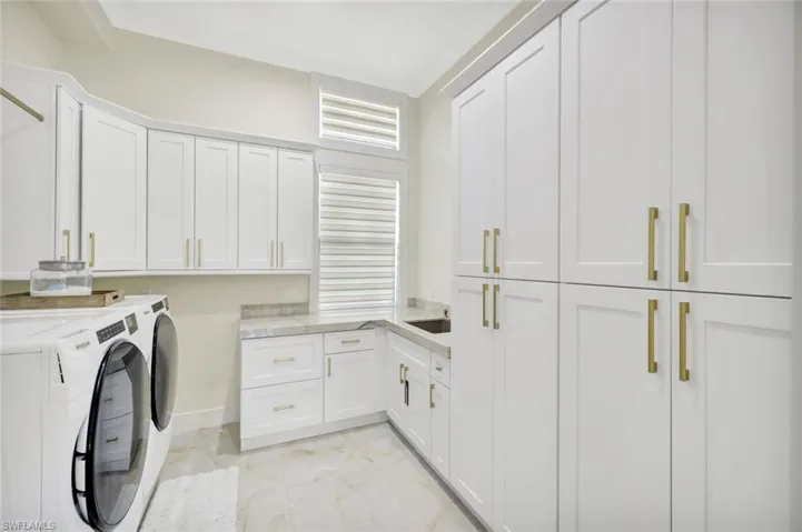 Laundry room with washer and clothes dryer, cabinet space, and light marble finish floors