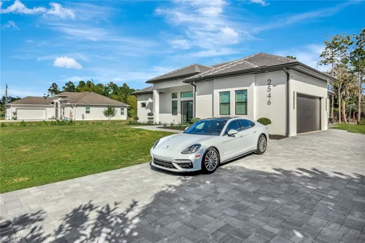 View of front of house with a garage, a front yard, stucco siding, and decorative driveway