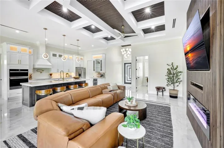 Living area with a fireplace, coffered ceiling, light marble finish flooring, a ceiling fan, and a chandelier