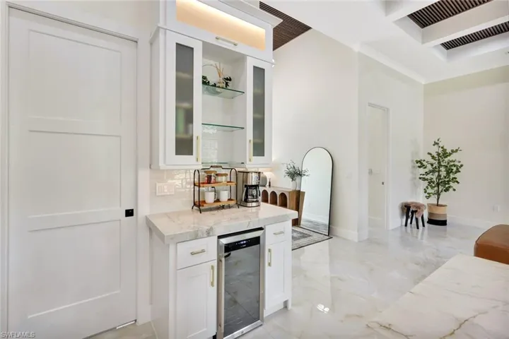 Bar featuring white cabinets, light stone countertops, wine cooler, glass insert cabinets, and light marble finish floors