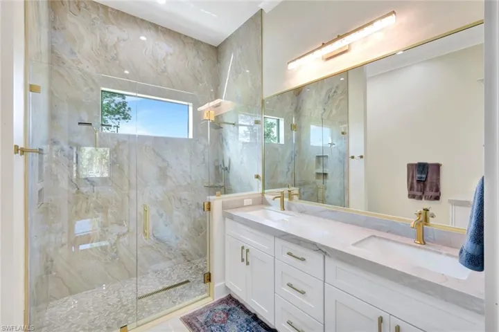 Full bath with double vanity and a marble finish shower