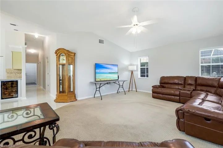 Living room featuring beverage cooler, vaulted ceiling, ceiling fan, and light carpet