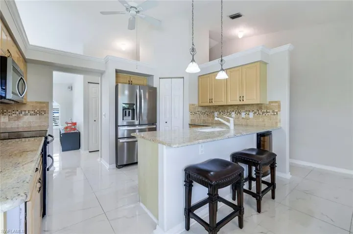 Kitchen featuring appliances with stainless steel finishes, ceiling fan, a peninsula, a kitchen bar, and tasteful backsplash