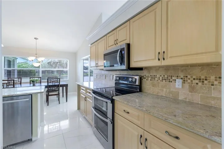 Kitchen featuring stainless steel appliances, light brown cabinetry, vaulted ceiling, tasteful backsplash, and a chandelier
