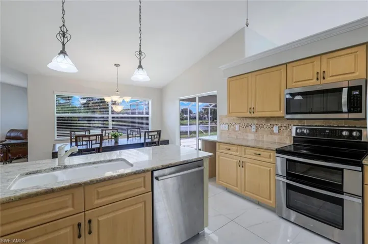 Kitchen featuring appliances with stainless steel finishes, light brown cabinetry, lofted ceiling, tasteful backsplash, and light stone countertops