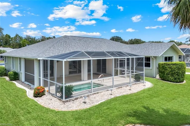 Rear view of property featuring a patio, a shingled roof, a lawn, an outdoor pool, and stucco siding