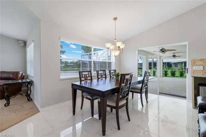 Dining area with lofted ceiling, light marble finish floors, a chandelier, and ceiling fan