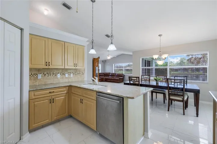 Kitchen featuring dishwasher, vaulted ceiling, light brown cabinets, light marble finish flooring, and a chandelier