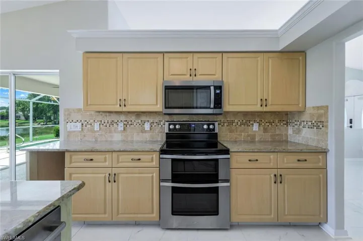 Kitchen with appliances with stainless steel finishes, light brown cabinets, light stone counters, light marble finish floors, and decorative backsplash