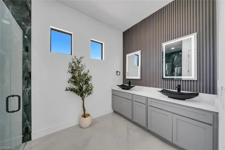 Full bath with double vanity, a shower stall, baseboards, and a sink