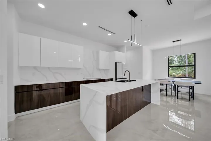 Kitchen with a sink, modern cabinets, light stone counters, white cabinetry, and a large island with sink