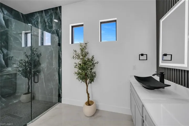 Bathroom featuring vanity, baseboards, and a marble finish shower