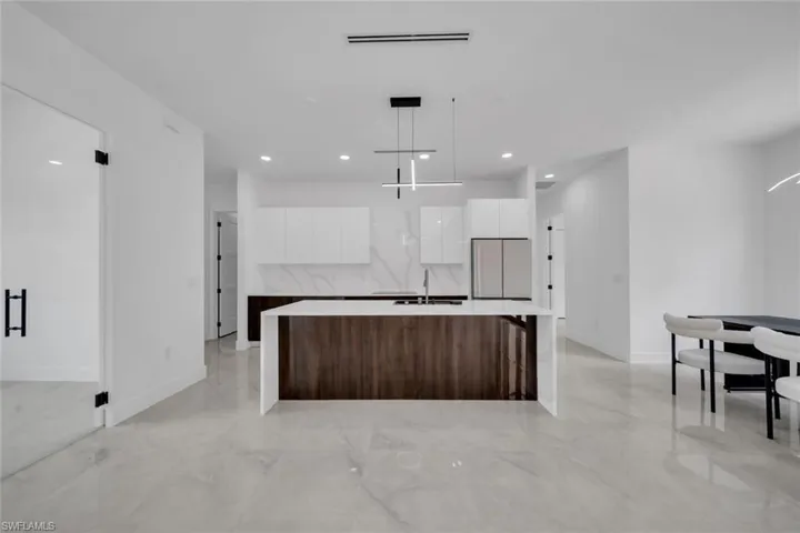 Kitchen with freestanding refrigerator, marble finish floor, white cabinets, a sink, and modern cabinets