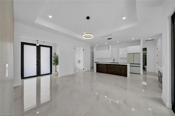 Unfurnished living room featuring a raised ceiling, french doors, recessed lighting, and a sink