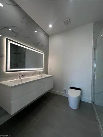 Full bath featuring double vanity, a marble finish shower, and recessed lighting