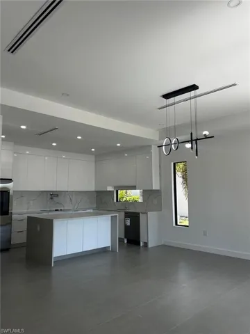 Kitchen with modern cabinets, backsplash, white cabinets, and light stone counters