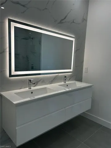 Bathroom with double vanity, a marble finish shower, and dark tile patterned floors