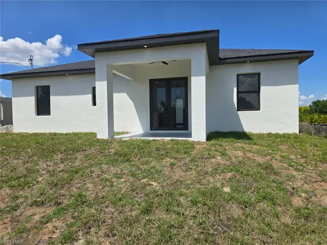 Rear view of property with a lawn and stucco siding