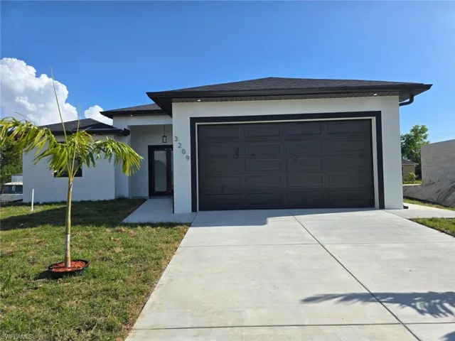 View of front of house featuring driveway, stucco siding, a front yard, and a garage