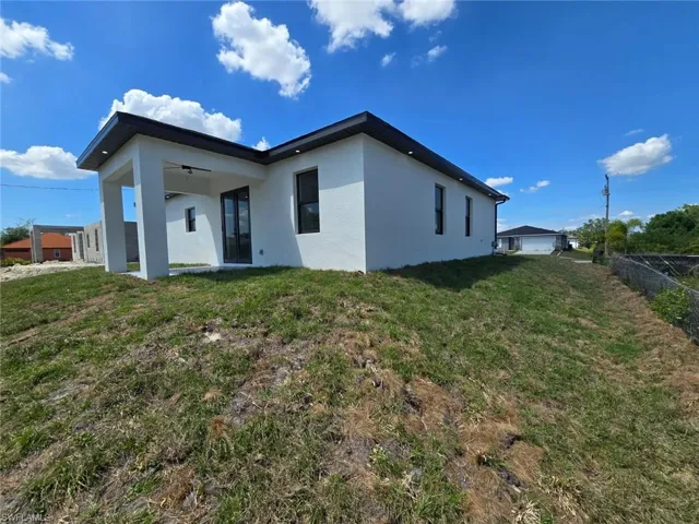 Rear view of house with a lawn, ceiling fan, stucco siding, and fence