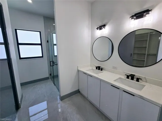 Full bath featuring baseboards, double vanity, a sink, and a stall shower
