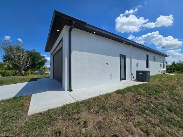 View of side of property with stucco siding, a garage, cooling unit, and a yard