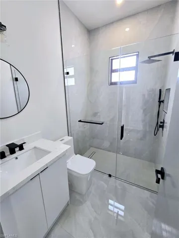 Bathroom featuring marble finish floor, toilet, a stall shower, and vanity