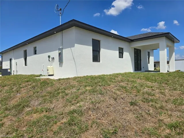 Rear view of house with a lawn, stucco siding, and central AC
