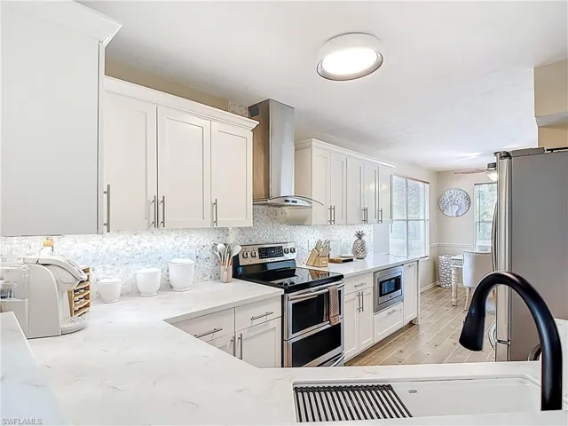 Kitchen with stainless steel appliances, white cabinetry, light wood-style floors, and backsplash
