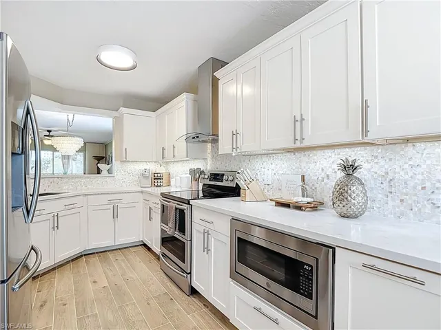 Kitchen featuring stainless steel appliances, white cabinetry, light wood-type flooring, and decorative backsplash