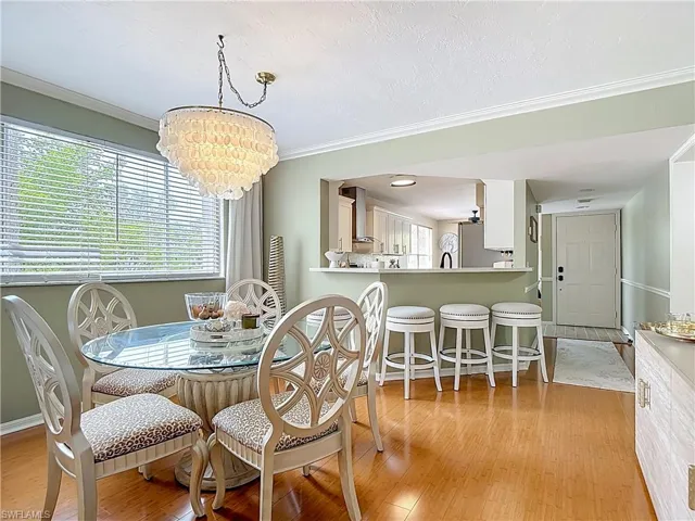 Dining room featuring light wood finished floors, a chandelier, ornamental molding, and a textured ceiling
