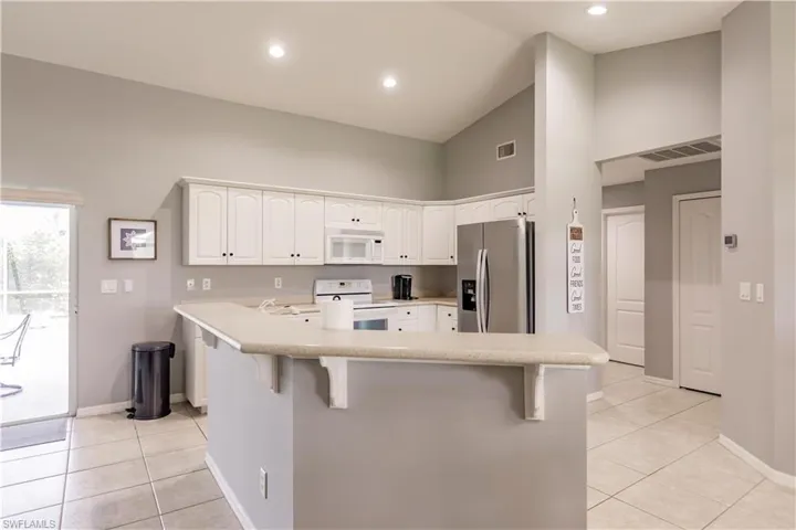 Kitchen with light tile patterned floors, high vaulted ceiling, white appliances, a kitchen bar, and kitchen peninsula