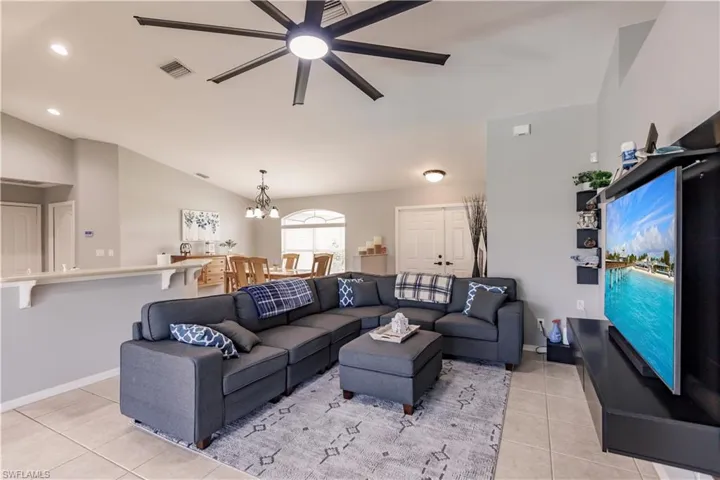 Living room featuring ceiling fan with notable chandelier, light tile patterned floors, and vaulted ceiling