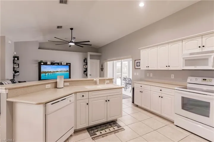 Kitchen featuring light tile patterned flooring, white cabinetry, white appliances, ceiling fan, and vaulted ceiling