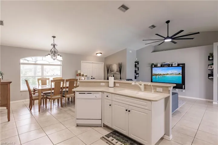 Kitchen with lofted ceiling, white cabinets, dishwasher, ceiling fan with notable chandelier, and decorative light fixtures