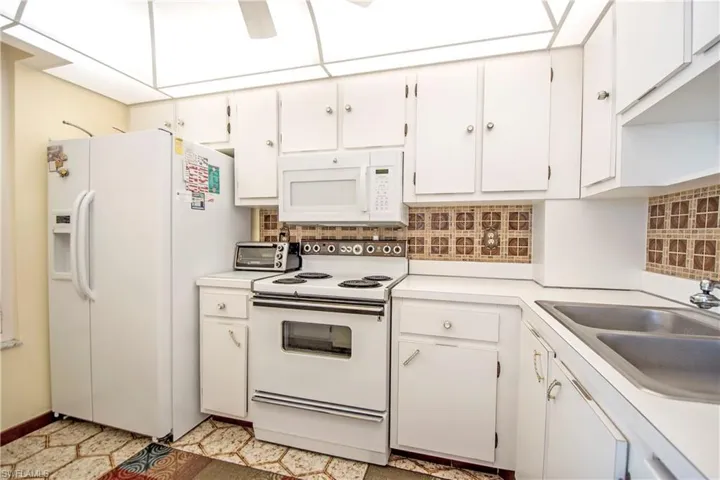 Kitchen featuring white appliances, light countertops, and white cabinetry