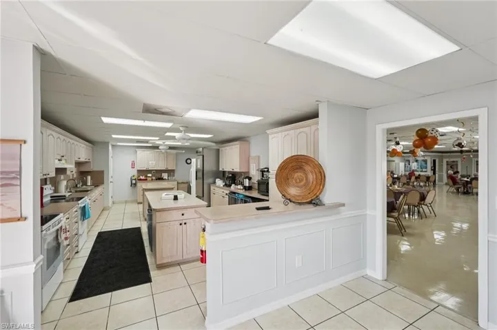 Kitchen with ceiling fan, light countertops, a center island, white electric stove, and a drop ceiling