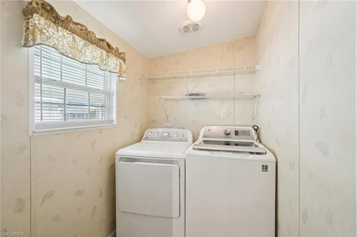 Laundry area featuring washer and clothes dryer, wallpapered walls, and lofted ceiling