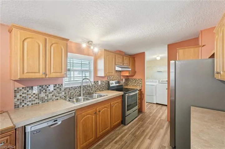 Kitchen with stainless steel appliances, backsplash, light countertops, washing machine and dryer, and light wood-style floors