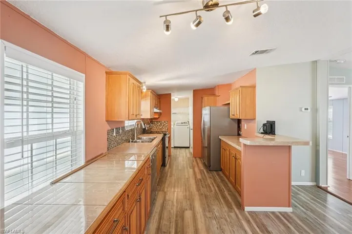 Kitchen featuring light wood-style flooring, tile countertops, stainless steel appliances, washer / clothes dryer, and a textured ceiling
