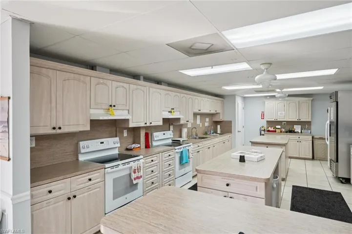 Kitchen with a kitchen island, white range with electric cooktop, light countertops, a ceiling fan, and a paneled ceiling