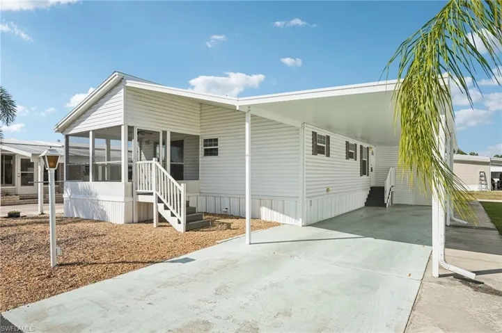 Manufactured / mobile home featuring driveway, an attached carport, entry steps, a sunroom, and a patio area