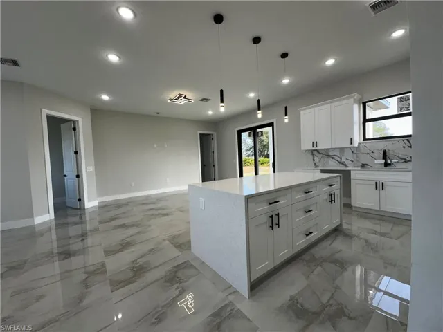 Kitchen with sink, decorative backsplash, decorative light fixtures, a kitchen island, and white cabinetry