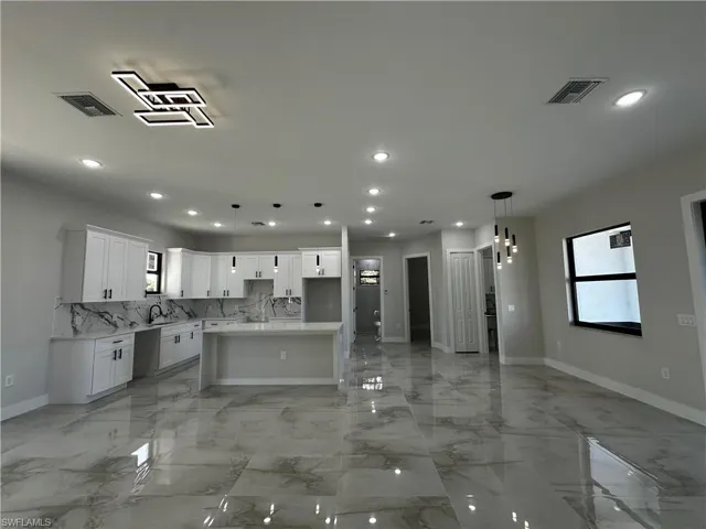 Kitchen with a center island, sink, hanging light fixtures, tasteful backsplash, and white cabinets