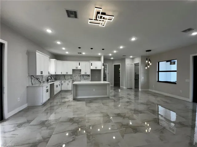 Kitchen with white cabinetry, sink, hanging light fixtures, tasteful backsplash, and a kitchen island