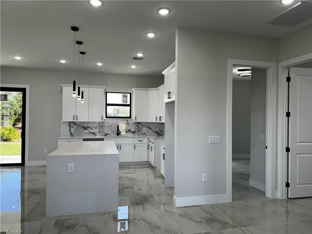 Kitchen featuring white cabinets, decorative light fixtures, a center island, and backsplash