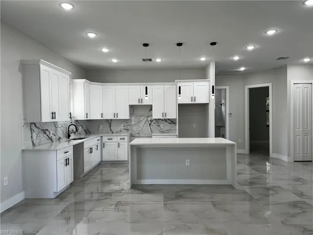 Kitchen with backsplash, a kitchen island, sink, pendant lighting, and white cabinetry