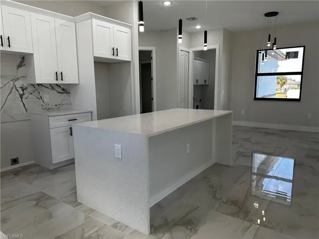 Kitchen featuring white cabinets, pendant lighting, a kitchen island, and backsplash