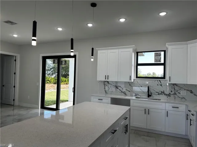 Kitchen featuring white cabinetry, sink, hanging light fixtures, and light stone counters